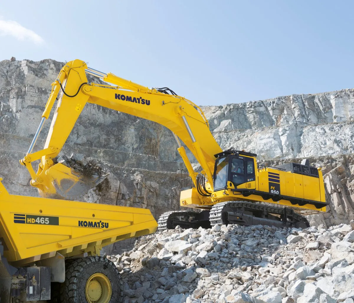 Excavator Komatsu PC950 memuat material batu ke dump truck menunjukkan spesifikasi alat berat seperti kapasitas bucket dan tenaga mesin